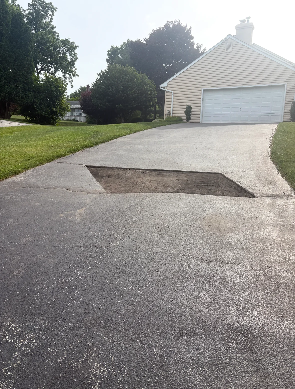 Asphalt driveway with patched pothole repair near residential garage