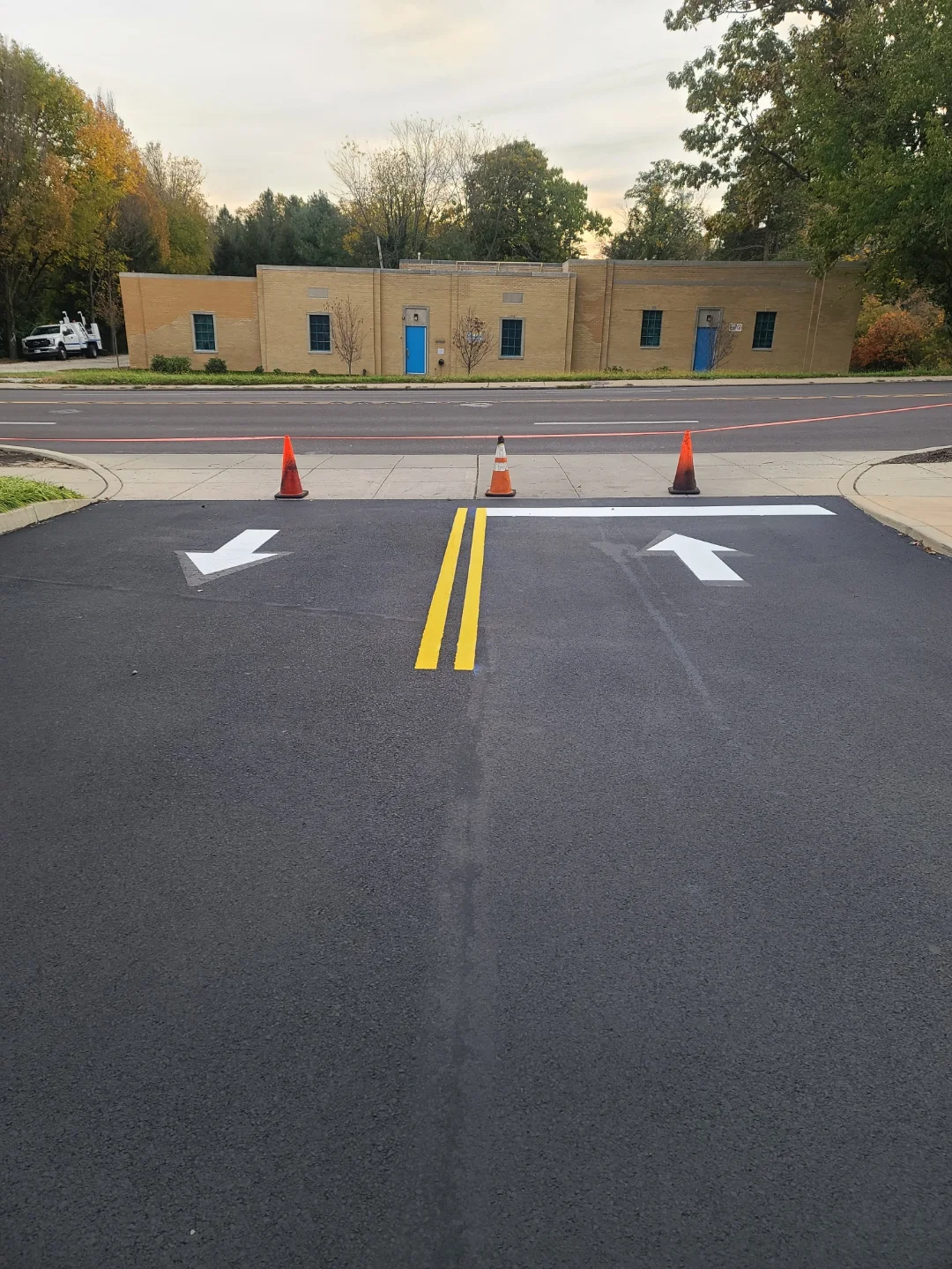 Newly striped asphalt parking lot with yellow center lines and white directional arrows in front of brick building