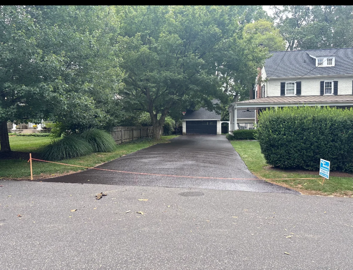 Newly sealcoated residential driveway with safety barriers and white colonial home