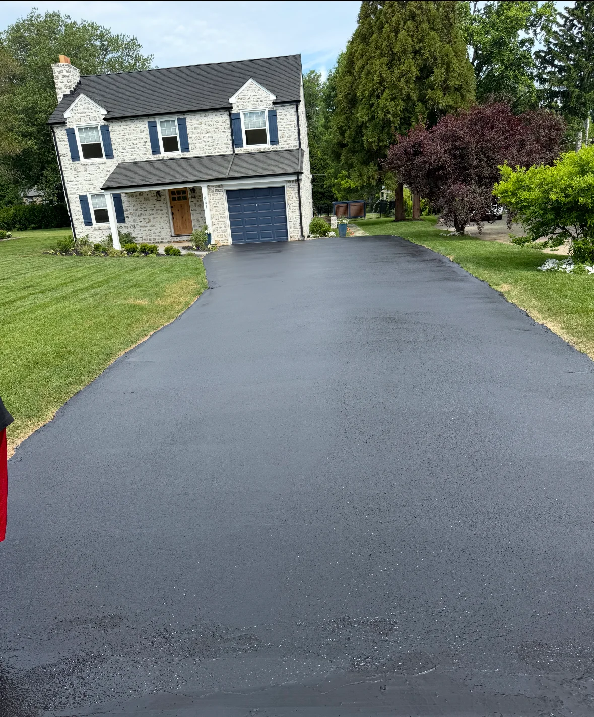 Newly sealcoated residential driveway with dark finish in front of stone home