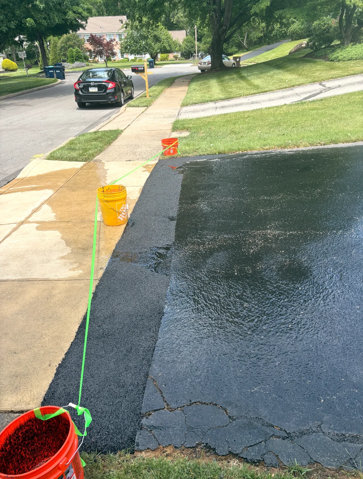 Freshly sealed asphalt driveway with patched repairs and green line marking