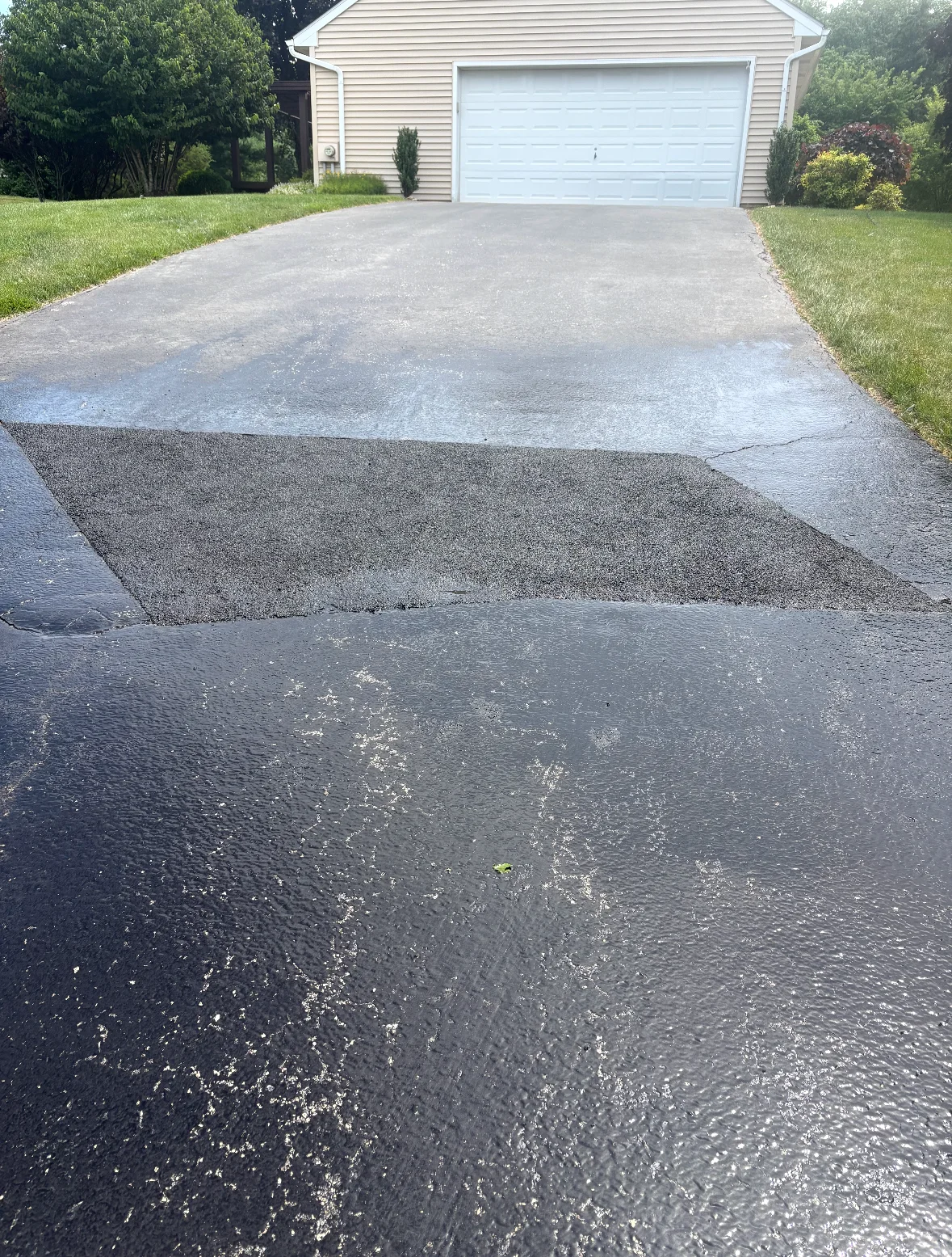 Asphalt driveway patch repair with new material applied to worn sections near garage