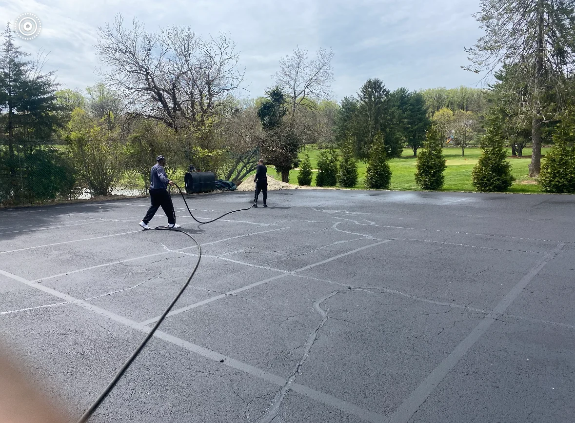 Crew applying sealcoat to marked residential driveway with landscaped grounds