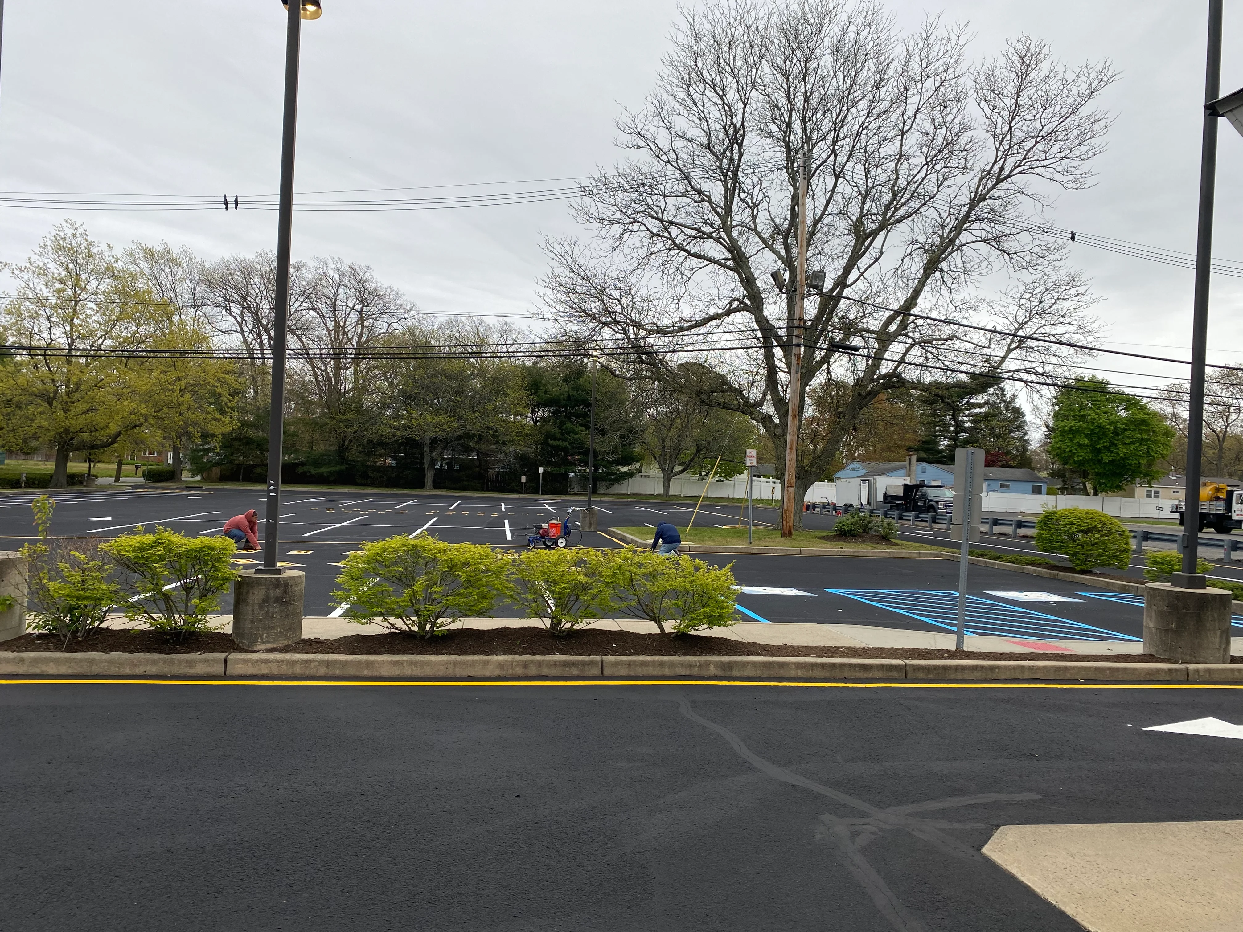 Commercial parking lot sealcoating in progress with white striping and landscaped medians