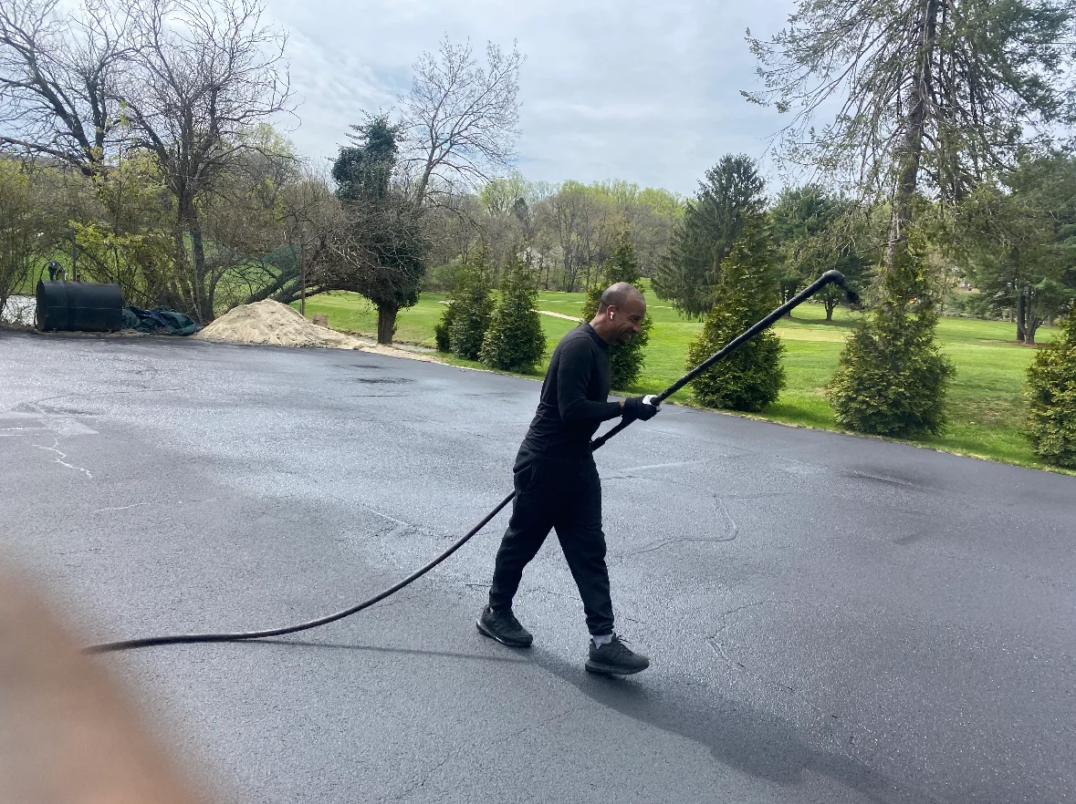 Technician applying sealcoat to asphalt driveway with push applicator